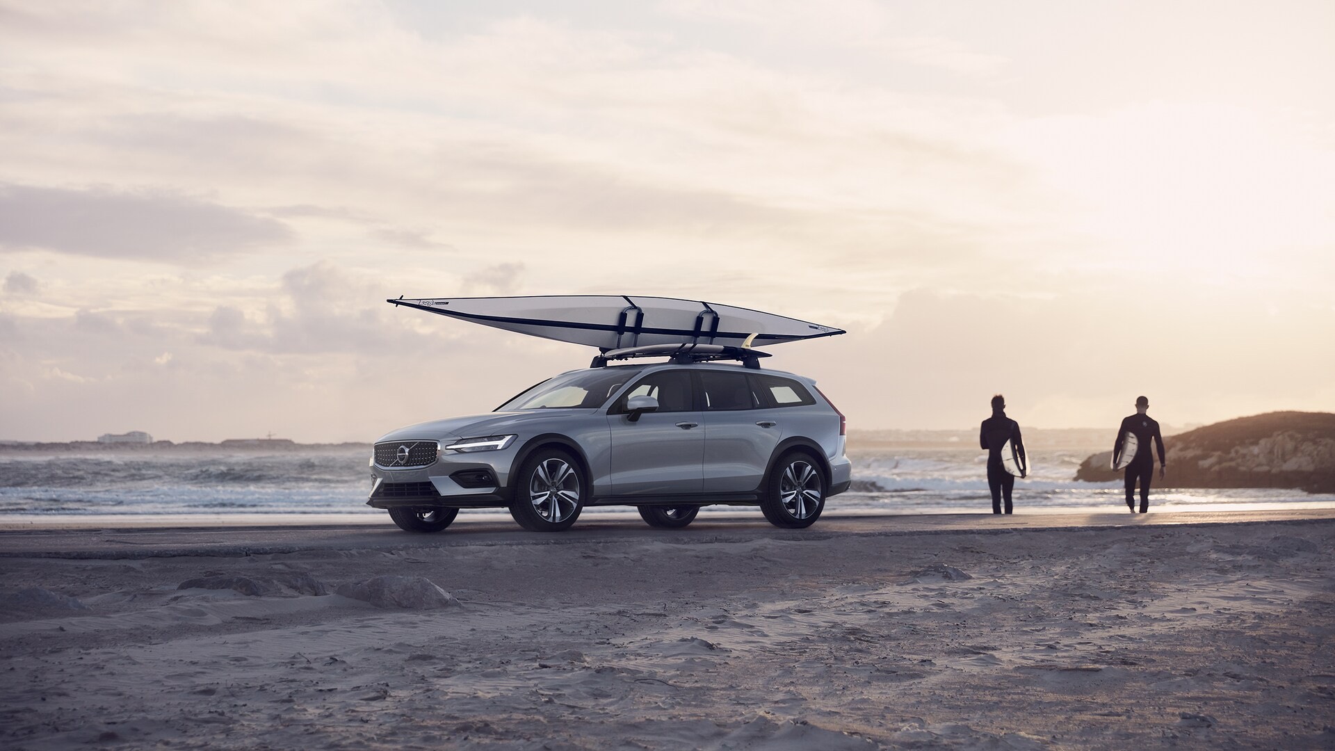 Vue latérale d'une Volvo V60 Cross-country 2022 sur la plage à côté de deux surfeurs