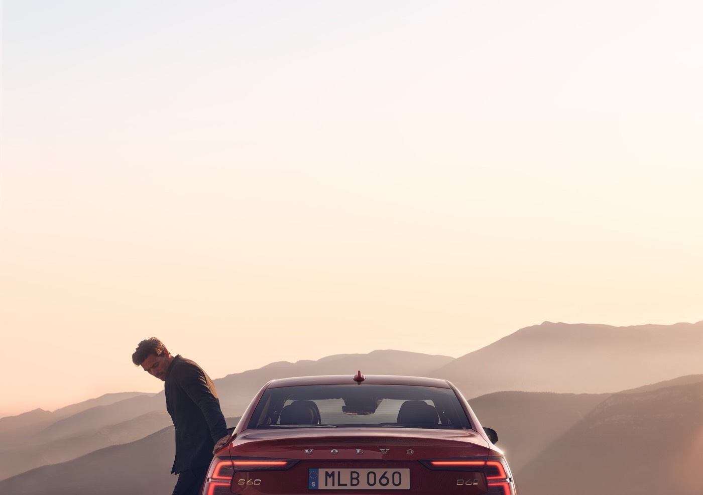 Vue arrière du Volvo S60 face aux montagnes avec homme accoté sur la porte du véhicule