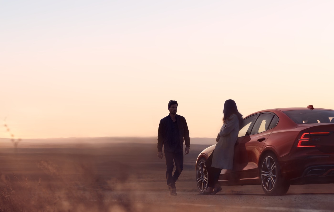 Un couple installé à côté de leur Volvo S60 2021 garé dans un paysage désertique de vision floue