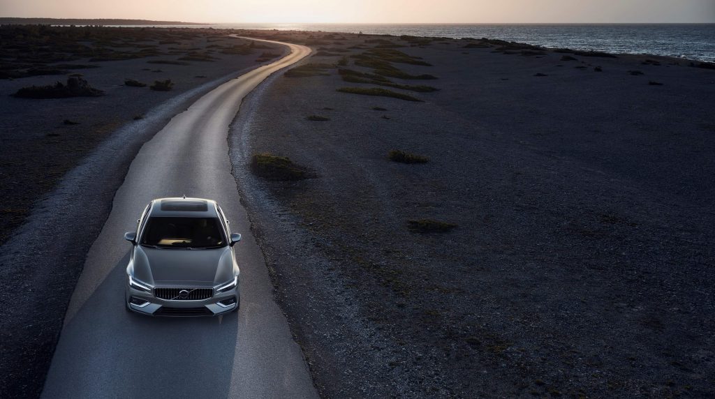 Vue de haut de la Volvo S60 Inscription 2021 Gris galet métallisé roulant sur un chemin étriot au bord de l'océan