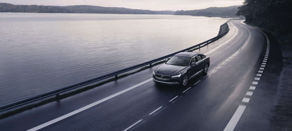 Volvo S90 Recharge T8 plug-in hybrid 2021 gris platine roulant sur l'autoroute au bord d'un grand lac