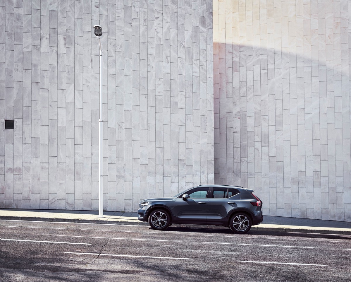 Vue éloignée et latérale du Volvo XC40 2022 couleur bleu denim garé en pente au long d'un mur